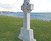 Diagonal View of Celtic Cross on green grass at waterfront, expansive lake in background.